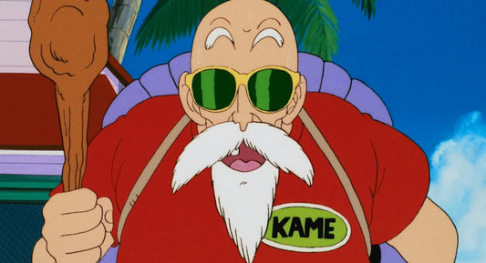 Tortue Géniale, lunettes à verres verts et bâton en main, porte une chemise rouge à écusson KAME et sa carapace violette sur le dos.